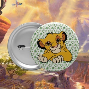 Puede incluir: Un botón redondo con un fondo verde y una imagen de dibujos animados de Simba, un cachorro de león, de la película de Disney El Rey León. Simba está mirando al espectador con una expresión seria. El botón está rodeado por un borde blanco.