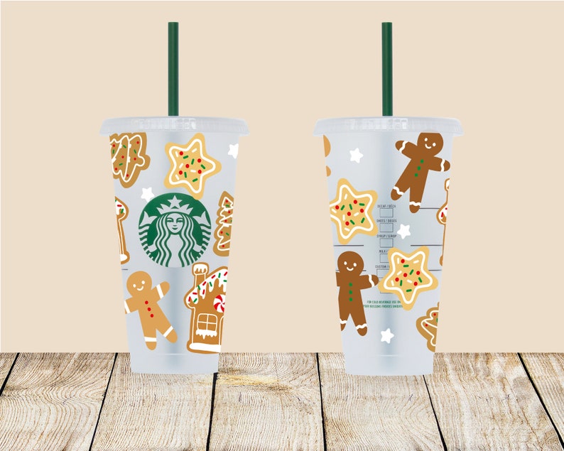 May include: Two clear plastic tumblers with green straws and a Christmas cookie design. The tumblers feature gingerbread men, star-shaped cookies, and a gingerbread house. One tumbler has the Starbucks logo.
