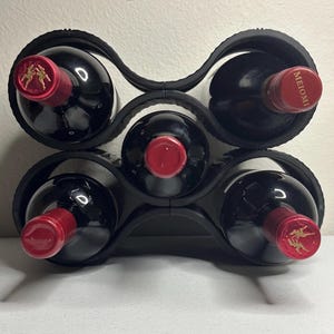May include: A black wine rack holding six bottles of red wine. The bottles have red caps and are arranged in two rows of three. The rack is made of a curved, interlocking design.