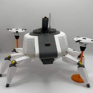 May include: A white and gray robotic spider with six legs, two disc-shaped antennae, and a central turret. The legs have yellow accents. The robot is set against a white background.