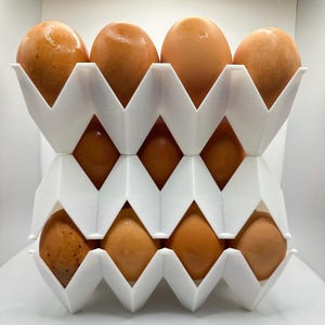 May include: A white, geometric egg holder filled with brown eggs. The holder is made of a series of zig-zag shaped compartments, designed to cradle each egg. The eggs are a warm brown colour, and the holder is clean and modern.