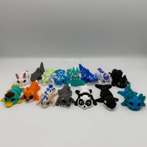 Puede incluir: Colección de figuras hechas a mano de arcilla polimérica de colores. El surtido incluye varios animales y criaturas fantásticas, como un panda, una orca, un conejo y figuras con forma de dragón. Cada figura tiene un diseño único.
