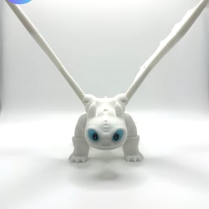 Könnte beinhalten: Eine weiße, 3D-gedruckte Drachenfigur mit großen Flügeln und leuchtend blauen Augen. Der Drache befindet sich in einer geduckten Position, mit weit ausgebreiteten Flügeln. Der Text "SABER 3D Authorized Seller" befindet sich in einem blauen Kreis.