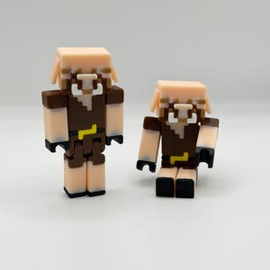 May include: Two block-style figurines, one large and one small, in a light tan, brown, black, and yellow color scheme. The figures have a square head, brown torso, and black feet and hands. The figures appear to be based on a video game character.