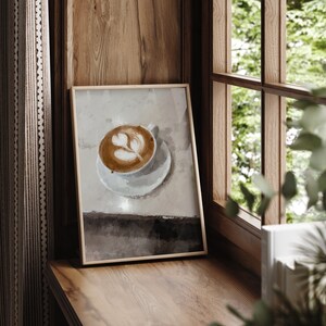 K&ouml;nnte beinhalten: Ein gerahmter Druck eines Latte mit einem Herzdesign in einer wei&szlig;en Tasse auf einem wei&szlig;en Unterteller. Der Hintergrund ist ein hellbrauner Aquarell-Wasch.