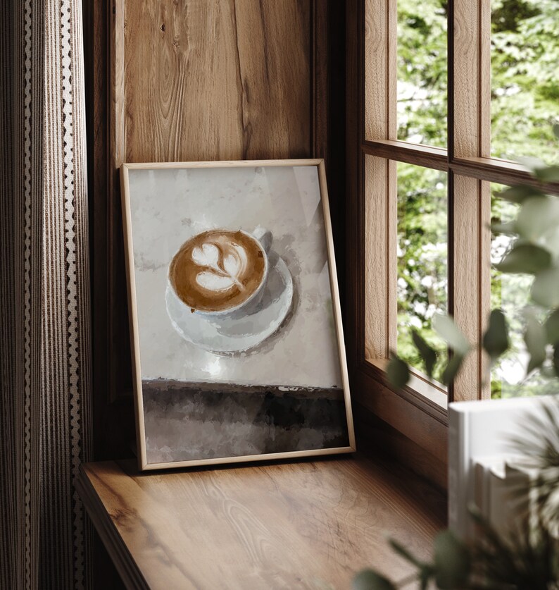 K&ouml;nnte beinhalten: Ein gerahmter Druck eines Latte mit einem Herzdesign in einer wei&szlig;en Tasse auf einem wei&szlig;en Unterteller. Der Hintergrund ist ein hellbrauner Aquarell-Wasch.