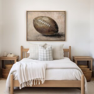 May include: A light wood bed frame with a white duvet and two pillows. A framed painting of a brown football is hanging on the wall above the bed.