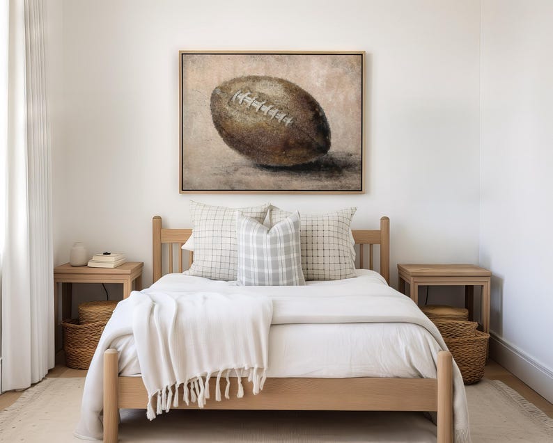 May include: A light wood bed frame with a white duvet and two pillows. A framed painting of a brown football is hanging on the wall above the bed.