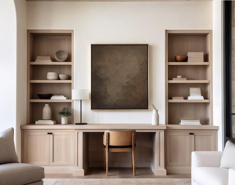 May include: A home office setup with built-in light wood shelving units flanking a desk. The desk has a wooden chair and a black lamp. A large abstract painting hangs above the desk, and decorative items are on the shelves.