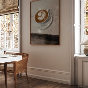 K&ouml;nnte beinhalten: Ein gerahmter Druck eines Latte-Art-Designs in einer wei&szlig;en Keramiktasse auf einem wei&szlig;en Unterteller. Der Hintergrund ist hellbraun.