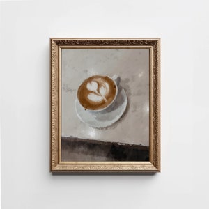 K&ouml;nnte beinhalten: Ein gerahmtes Gem&auml;lde einer Tasse Kaffee mit Latte-Art-Design. Der Kaffee befindet sich in einer wei&szlig;en Tasse und Untertasse auf einer hellbraunen Oberfl&auml;che. Der Rahmen ist golden mit verzierten Details.