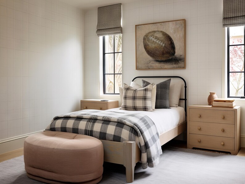 May include: A bedroom with a white and black plaid blanket on a bed with a black metal frame. There is a brown football painting on the wall above the bed. There is a light pink ottoman in the foreground.