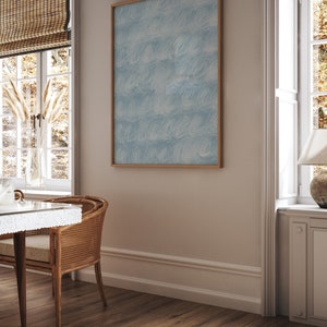 May include: A framed abstract painting with a blue and white pattern hangs on a light beige wall in a room with a wooden floor and a window with blinds.