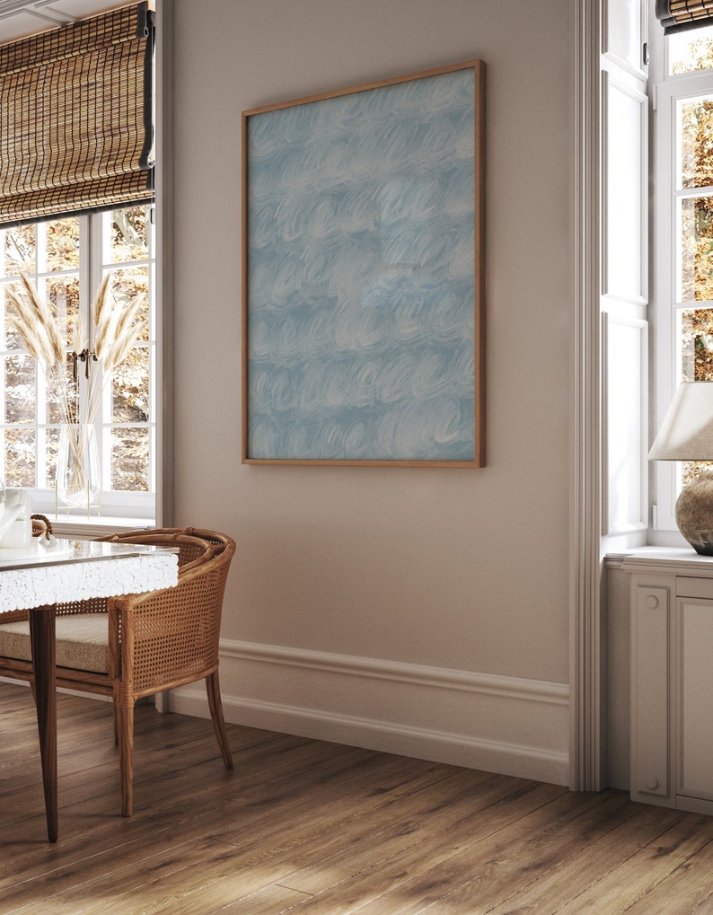 May include: A framed abstract painting with a blue and white pattern hangs on a light beige wall in a room with a wooden floor and a window with blinds.