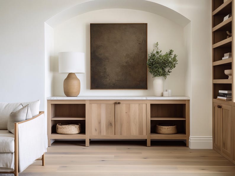 May include: A light wood cabinet with open shelving and closed doors, topped with a marble surface. A large framed abstract art piece hangs above the cabinet. A lamp with a beige base and white shade sits on the cabinet.