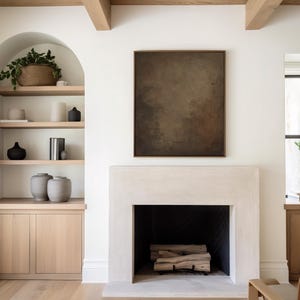 May include: A modern living room with a fireplace and built-in shelving. The fireplace is white with a black interior and stacked firewood. A large abstract painting hangs above the fireplace. Shelves display vases, books, and decorative items.
