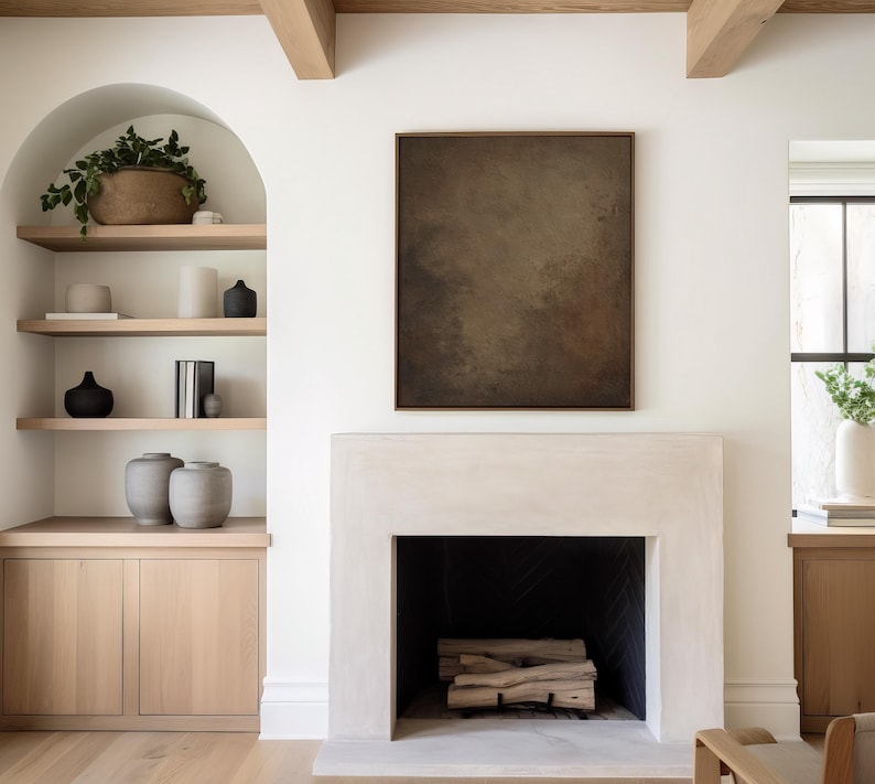 May include: A modern living room with a fireplace and built-in shelving. The fireplace is white with a black interior and stacked firewood. A large abstract painting hangs above the fireplace. Shelves display vases, books, and decorative items.
