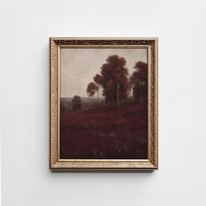 May include: A framed landscape painting featuring a dark, moody field with deep red and brown tones under a cloudy sky. A cluster of trees with autumn-coloured foliage stands on a gentle hill. The artwork is enclosed in an ornate, metallic gold frame.