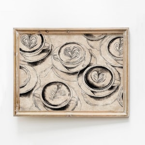 Op de afbeelding: Een ingelijste print met een herhalend patroon van koffiekopjes met latte art. De kopjes en schotels zijn in zwart-wit geschetst, met hart- en bladmotieven in de koffie. De lijst is lichtbruin.