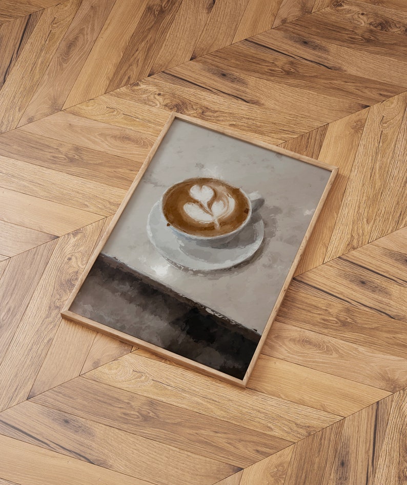 K&ouml;nnte beinhalten: Ein gerahmtes Gem&auml;lde einer Tasse Kaffee mit Latte-Art-Design. Der Kaffee befindet sich in einer wei&szlig;en Tasse und Untertasse auf einer hellgrauen Oberfl&auml;che.