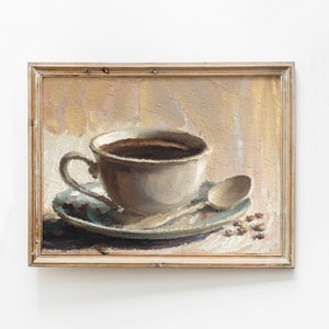 Op de afbeelding: Een ingelijst olieverfschilderij van een witte koffiekop met een schoteltje en een lepel. De kop is gevuld met donkerbruine koffie en het schoteltje heeft een lichtblauw en wit patroon. De achtergrond is lichtbruin en beige.