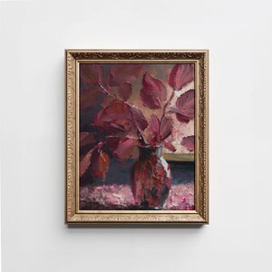 May include: A framed oil painting of a still life featuring a vase filled with deep red leaves. The vase is a muted blue and white color and sits on a pink and white patterned surface. The painting is framed in a gold ornate frame.
