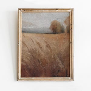 Puede incluir: Una pintura enmarcada de un paisaje con un campo de hierba alta en primer plano, una masa de agua distante y algunos árboles en el fondo. La pintura está realizada en tonos apagados de marrón, beige y gris.