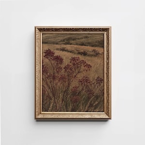 May include: A framed landscape painting featuring dark red wildflowers in the foreground set against a field of golden-brown grasses and rolling hills in the distance. The artwork is enclosed in an ornate, metallic gold-toned rectangular frame.