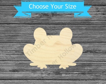May include: A wooden frog-shaped cutout with a light wood grain finish. The cutout has a rounded head and body with visible feet. A blue banner above the frog reads "Choose Your Size". The background is a gray wooden surface.