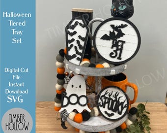 May include: A Halloween tiered tray set featuring a black cat, coffin, and ghost decorations. The set includes a mug and decorative accents. The tray is decorated with orange, grey, and black felt balls. The word "SPOOKY" is visible.