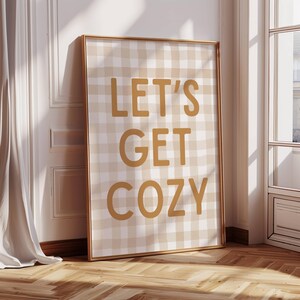 Könnte beinhalten: Ein gerahmter Druck mit einem beige-weiß karierten Hintergrund. Der Text "LET'S GET COZY" ist in senfgelber Farbe gedruckt.