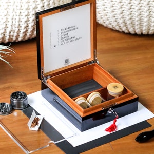 May include: A black wooden box with a red tassel and a lock. The box is open and has a wooden interior with three small glass jars. The box is labeled with the words "Persistence, Determination, Grind, Hustle, No Excuses, All of the above".