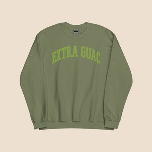 Könnte beinhalten: Ein grüner Pullover mit dem Text "EXTRA GUAC" in einem grünen Bogen auf der Vorderseite.