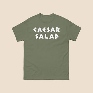 May include: A green t-shirt with white text that reads "CAESAR SALAD" in a stylized font.