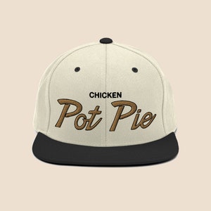 Puede incluir: Una gorra de béisbol blanca y negra con un logotipo bordado en marrón que dice "Chicken Pot Pie".