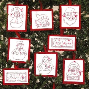 May include: A collection of seven white fabric ornaments with red embroidered outlines and details. The designs include snowmen, a Santa face, and rectangular signs with the text Flakes Welcome, Think Snow, and Snow Happens, all with red borders.
