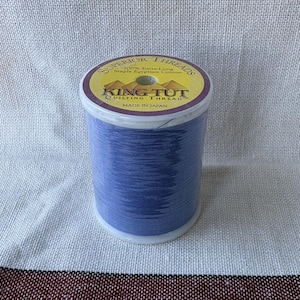 Op de afbeelding: Een spoel blauw quiltgaren met een geel en paars etiket met de tekst "SUPERIOR THREADS" en "KING TUT QUILTING THREAD". Het garen is gemaakt van 100% extra lange Egyptische katoen. Gemaakt in Japan.
