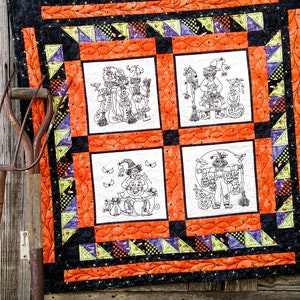 May include: A Halloween quilt with four embroidered panels featuring witches, cats, pumpkins, and other Halloween imagery. The quilt is made with orange, black, green, and purple fabrics and has a black and white checkered border.