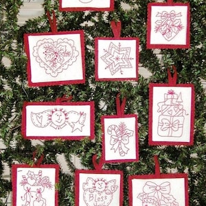 Pode incluir: Uma coleção de nove ornamentos retangulares de tecido branco com bordas de feltro vermelho e desenhos bordados em vermelho, incluindo um pássaro, azevinho, um floco de neve, presentes, uma bengala doce, uma meia, um coração com o texto Bless You e sinos.