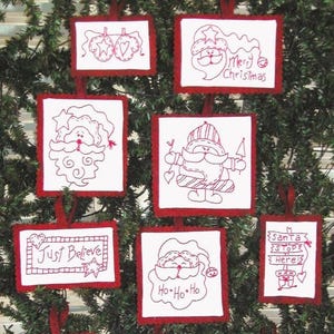 May include: A set of seven rectangular white fabric ornaments with red scalloped edges and red embroidered designs. The designs include Santa Claus faces, mittens, and text reading Merry Christmas, Just Believe, Ho Ho Ho, and Santa Stop Here.