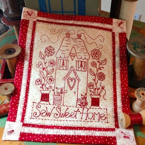 May include: Red and white quilted wall hanging with a red embroidered house and the text "Sew Sweet Home".