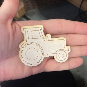 May include: A wooden cutout of a tractor with a simple design. The tractor is brown and has a white window.