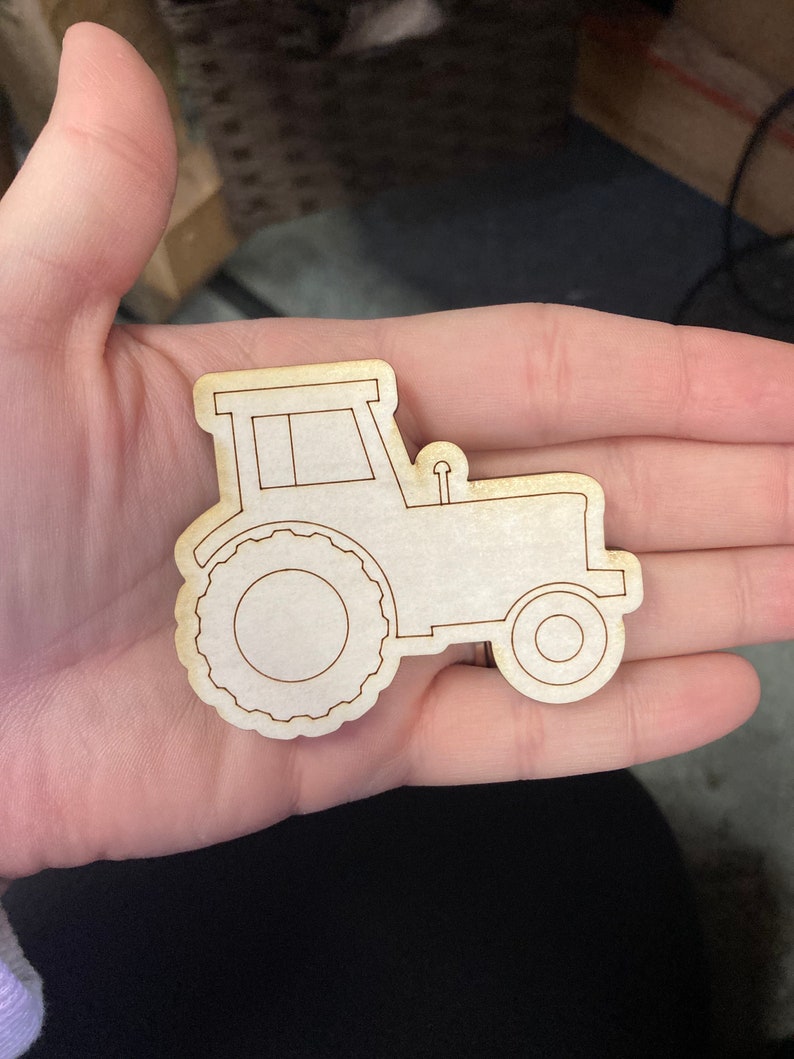 May include: A wooden cutout of a tractor with a simple design. The tractor is brown and has a white window.