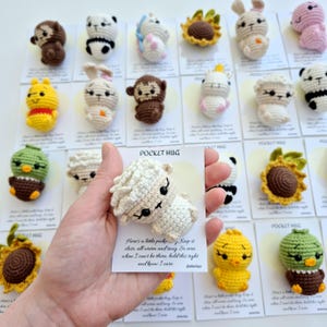 以下が含まれることがあります： パンダ、ウサギ、サル、ヒヨコなど、手作りの編みぐるみ動物フィギュアのコレクション。各フィギュアは「POCKET HUG」と書かれたカードに表示されています。フィギュアは白、茶色、黄色、緑など、さまざまな色があります。