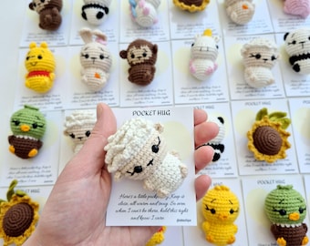 May include: A collection of handmade crochet animal figures, including a panda, bunny, monkey, and chick. Each figure is displayed on a card that reads "POCKET HUG". The figures are in various colors, such as white, brown, yellow, and green.