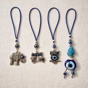 May include: Four blue and silver charm pendants with blue cords. The charms include an elephant, two owls, a single owl, and a blue fish with a large blue eye. Each charm has a blue eye design.