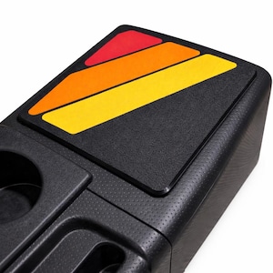 May include: Black console organizer with a colorful geometric design. The top features a red, orange, and yellow pattern. The organizer has a textured surface and includes a cup holder.