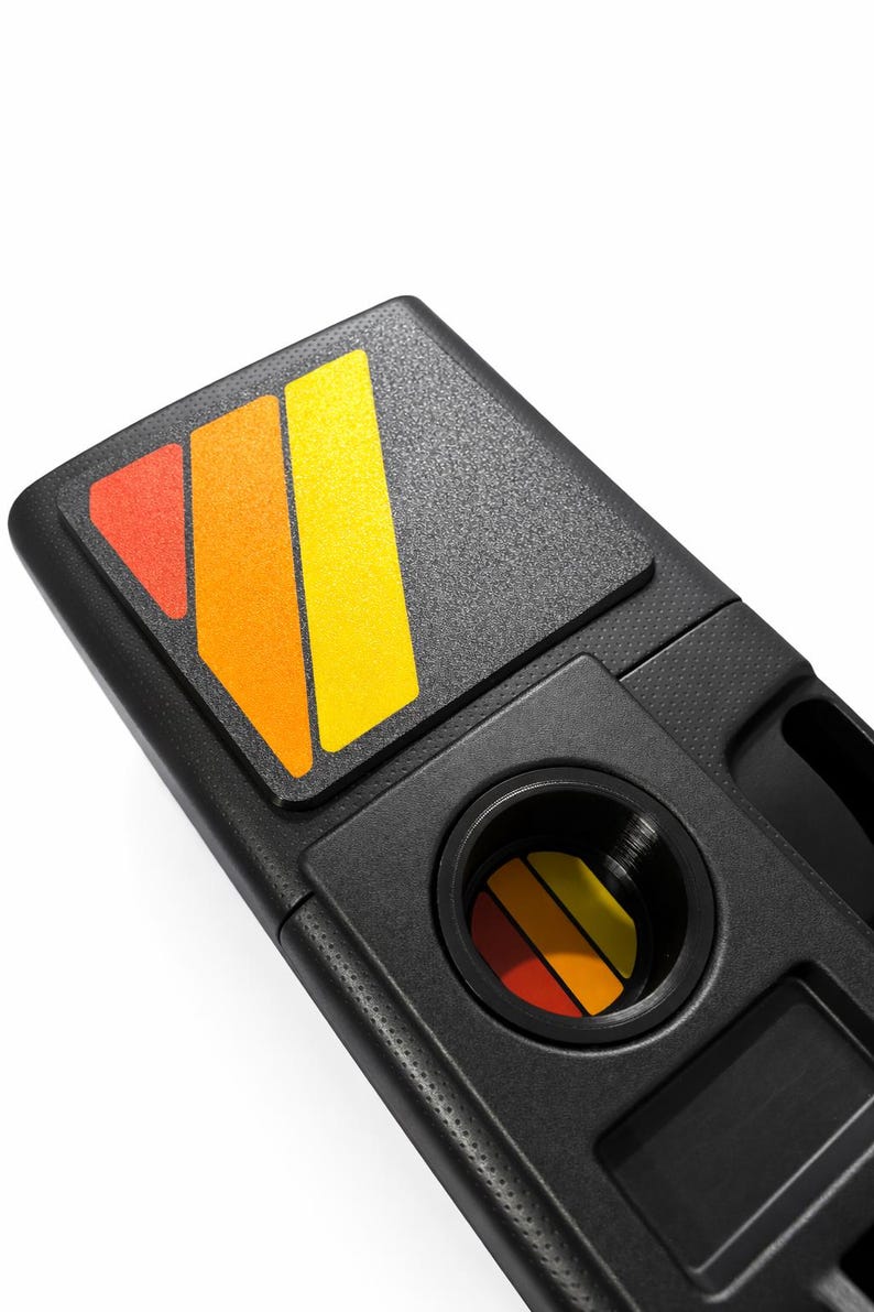 Pu&ograve; includere: Console per auto in plastica nera con superficie strutturata. &Egrave; dotata di un portabicchieri e di un vano rettangolare. La console &egrave; decorata con una grafica colorata nelle tonalit&agrave; del rosso, arancione e giallo.