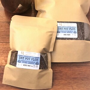 May include: Three tan paper bags of "Dry Pot Plus" organic compost and natural mineral, with a small succulent plant in a decorative wooden pot. The bags have labels with product information and are on a wooden surface.