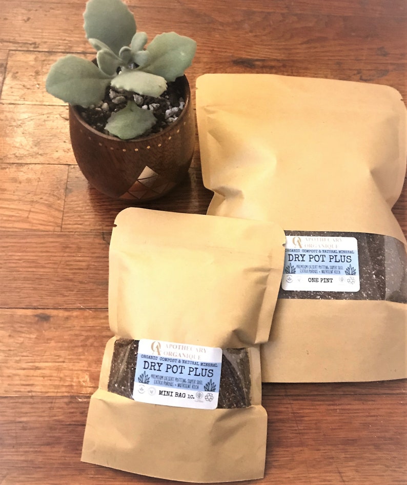 May include: Three tan paper bags of "Dry Pot Plus" organic compost and natural mineral, with a small succulent plant in a decorative wooden pot. The bags have labels with product information and are on a wooden surface.